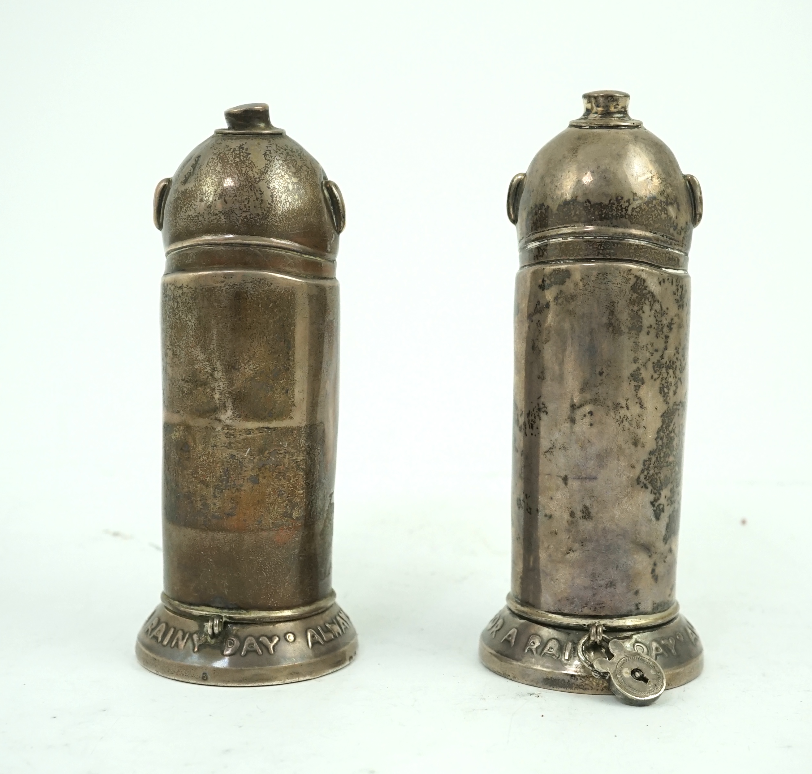 A matched pair of George V novelty silver money boxes, each cylindrical box embossed as a banker with an umbrella, the circular base inscribed 'Always be prepared for a rainy day'